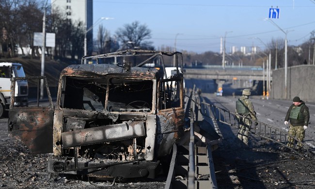 Ukrajinští vojáci stojí u shořelého vozidla Ukrajinské armády na západ od metropole Kyjeva, 26. února 2022. Ukrajina s Ruskem chtějí vést jednání na bělorusko-ukrajinské hranici. Photo: AFP