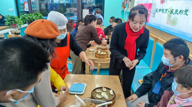 Snímek: Xu Xu (uprostřed) ukazuje, jak se vyrábí knedlíky během školení v restauraci paní Wang Chunzhi; 29. listopadu 2021. / Xu Xu