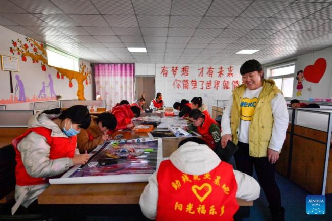 Η Τιεν Λιτσάο καθοδηγεί μερικούς νέους με ειδικές ανάγκες να φτιάξουν διακοσμητικούς πίνακες σε ένα κέντρο απασχόλησης για άτομα με ειδικές ανάγκες στην περιοχή Μπαοντί, στο Τιεντζίν της βόρειας Κίνας, σε φωτογραφία από την 1η Μαρτίου 2022. [Xinhua/Sun Fanyue]