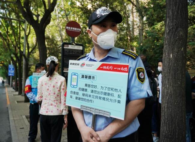 Ένα μέλος του προσωπικού της δημόσιας συγκοινωνίας του Πεκίνου κρατά μια πινακίδα για να υπενθυμίζει στους επιβάτες να δείχνουν τους κωδικούς υγείας QR σε μια στάση λεωφορείου στο Πεκίνο, πρωτεύουσα της Κίνας, 17 Μαΐου 2022. 