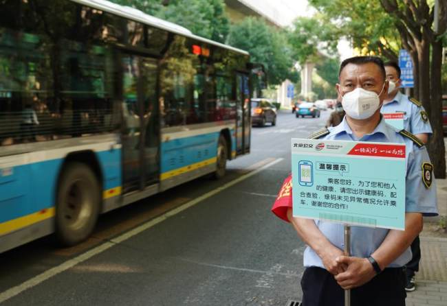 Τα μέλη του προσωπικού των μέσων μαζικής μεταφοράς του Πεκίνου κρατούν πινακίδες για να υπενθυμίζουν στους επιβάτες να δείχνουν κωδικούς QR υγείας σε στάση λεωφορείου στο Πεκίνο, πρωτεύουσα της Κίνας, 17 Μαΐου 2022. 