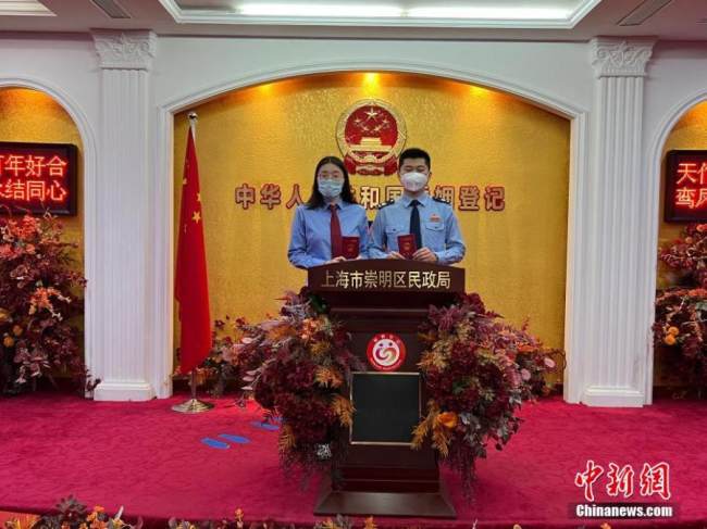 Οι νεόνυμφοι ποζάρουν για μια φωτογραφία με τα πιστοποιητικά του γάμου σε ένα κέντρο εγγραφής γάμων στην περιοχή Τσαομίνγκ, στη Σαγκάη της ανατολικής Κίνας, 20 Μαΐου 2022. (Φωτογραφία: China News Service) 