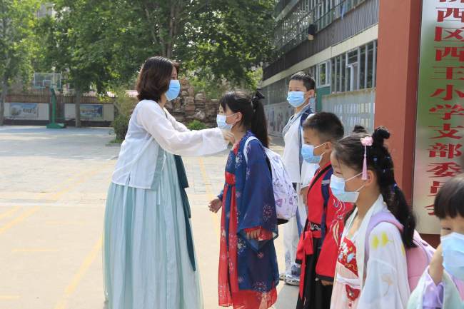 Μια δασκάλα, στο Δημοτικό Σχολείο Σιγουάνγκ του Τσιαοσί στην πρωτεύουσα Σιτζιατζουάνγκ της επαρχίας Χεμπέι, βοηθά τους μαθητές να φορέσουν σωστά το χάνφου τους. [Η φωτογραφία παρέχεται στο chinadaily.com.cn]