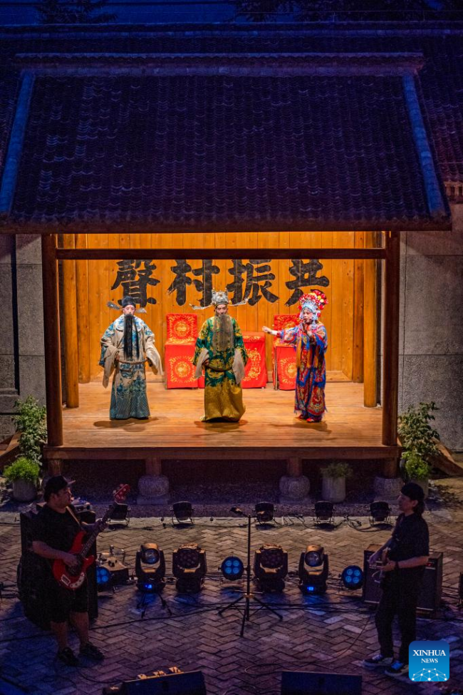 Μέλη ενός τοπικού θιάσου όπερας και μέλη ενός ροκ συγκροτήματος παίζουν μαζί στο χωριό Ντανανπό της κομητείας Χιουγού στην πόλη Τζιαοζουό, στην επαρχία Χενάν της κεντρικής Κίνας. 31 Ιουλίου 2022. 
